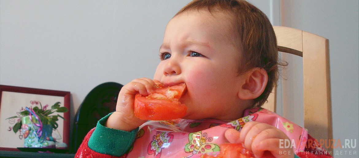 Ребёнок ест красный помидор